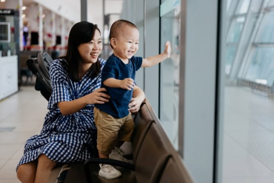 Smiling woman and child enjoying airport observation window, emphasizing international health and travel insurance coverage.