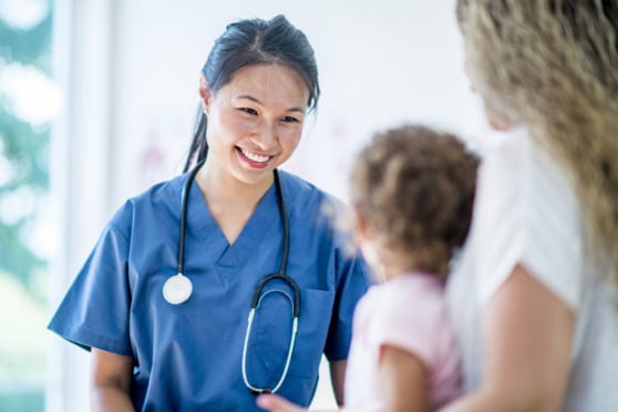 A friendly nurse in scrubs offering compassionate care to a mother and her young child in a clinical setting.