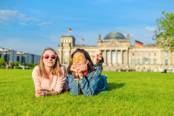 Enjoy two young women relaxing on the grass in Berlin, showcasing the importance of international health insurance while traveling abroad.