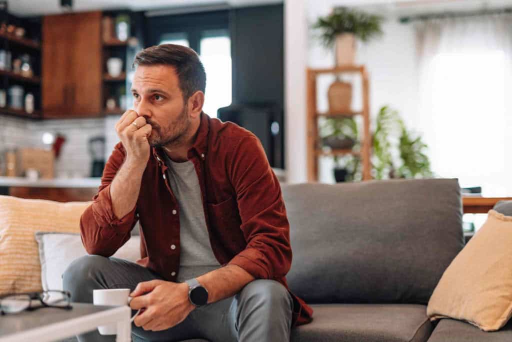 Worried man sitting on sofa at home biting his fingernails