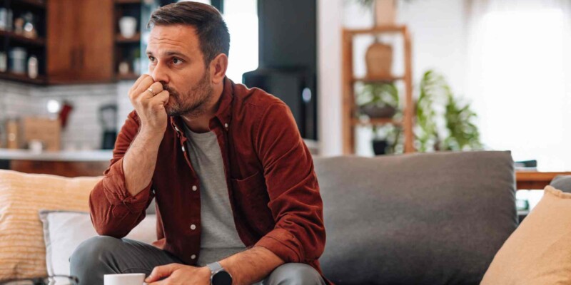 Worried man sitting on sofa at home biting his fingernails
