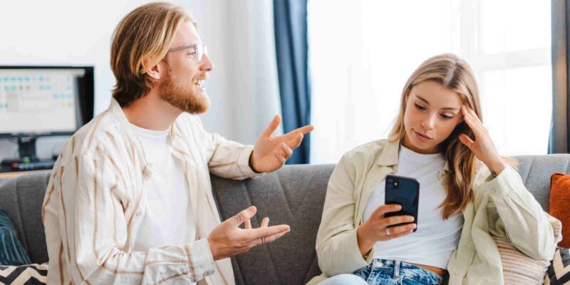 a young man explaining something to a woman who is not listening and instead using smartphone at home