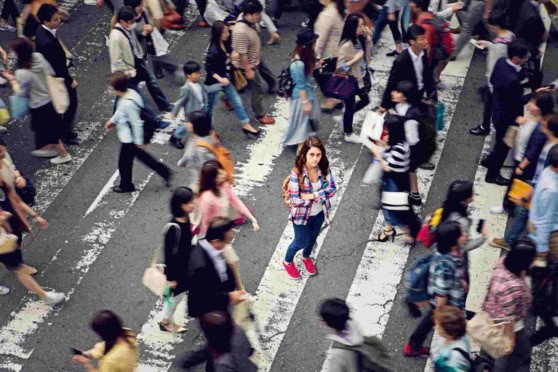 Aerial shot of a busy city street with people crossing at a pedestrian crosswalk, highlighting urban diversity and the need for reliable international health insurance coverage.