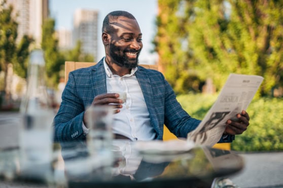 A professional man sitting outside in a park, reading a newspaper while holding a coffee cup, symbolizing international citizens, global connectivity, and confidence in global insurance solutions.