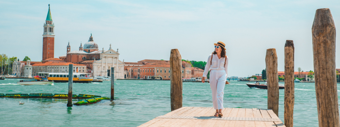 Beautiful woman walking on a dock with Venice's historic buildings and canals in the background, representing travel and insurance coverage abroad.