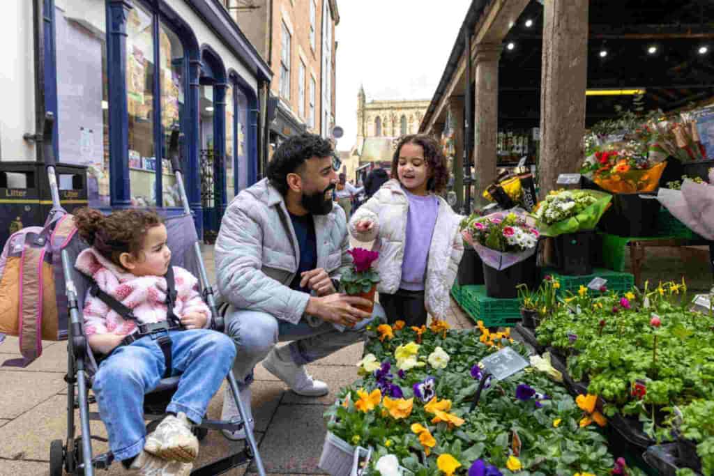 a father shopping at an outdoor market with his children, exploring his new home country, showing one of the ways you can help your child adjust to life abroad