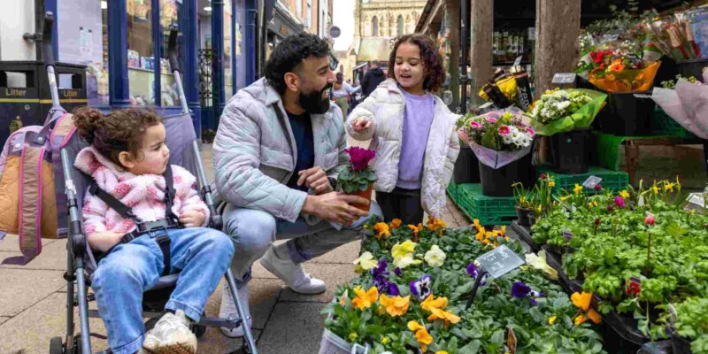 a father shopping at an outdoor market with his children, exploring his new home country, showing one of the ways you can help your child adjust to life abroad