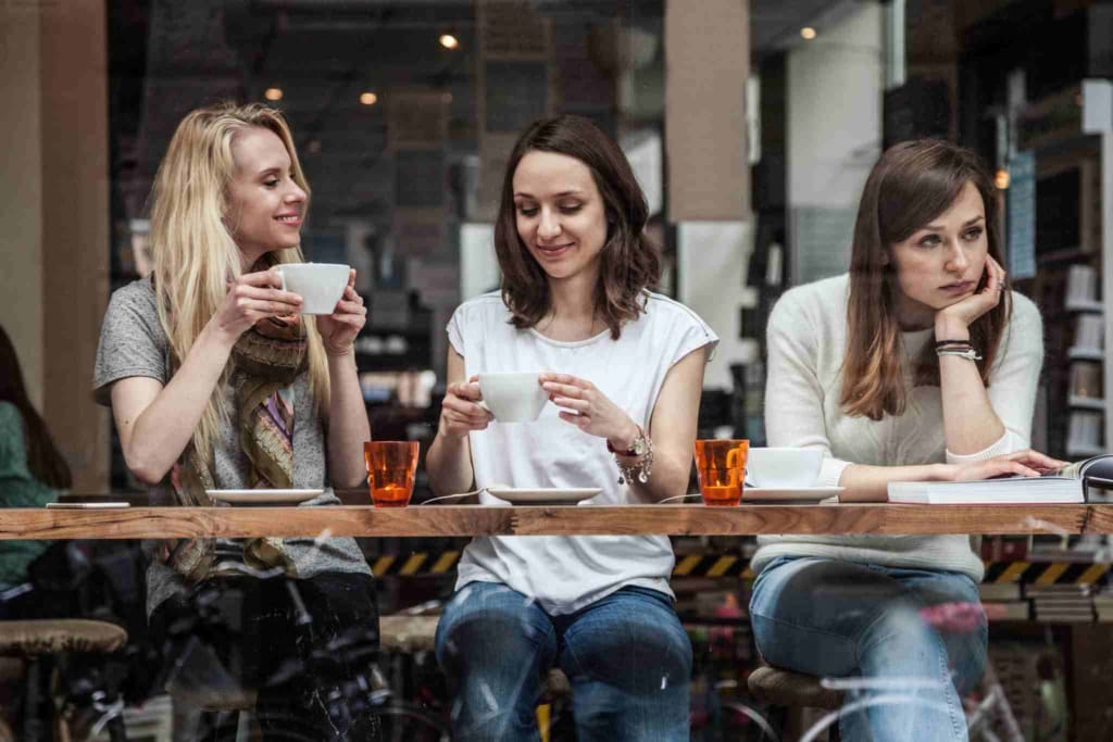 Friendly women sharing coffee and engaging in conversation at a modern cafe setting.