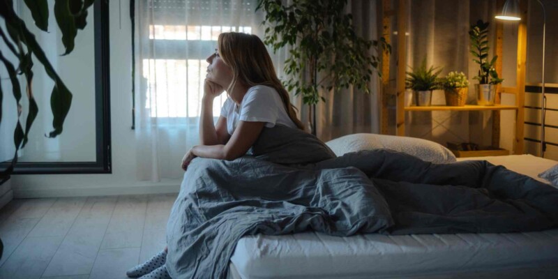 a woman sitting at the end of her bed during the night, struggling with culture shock related insomnia
