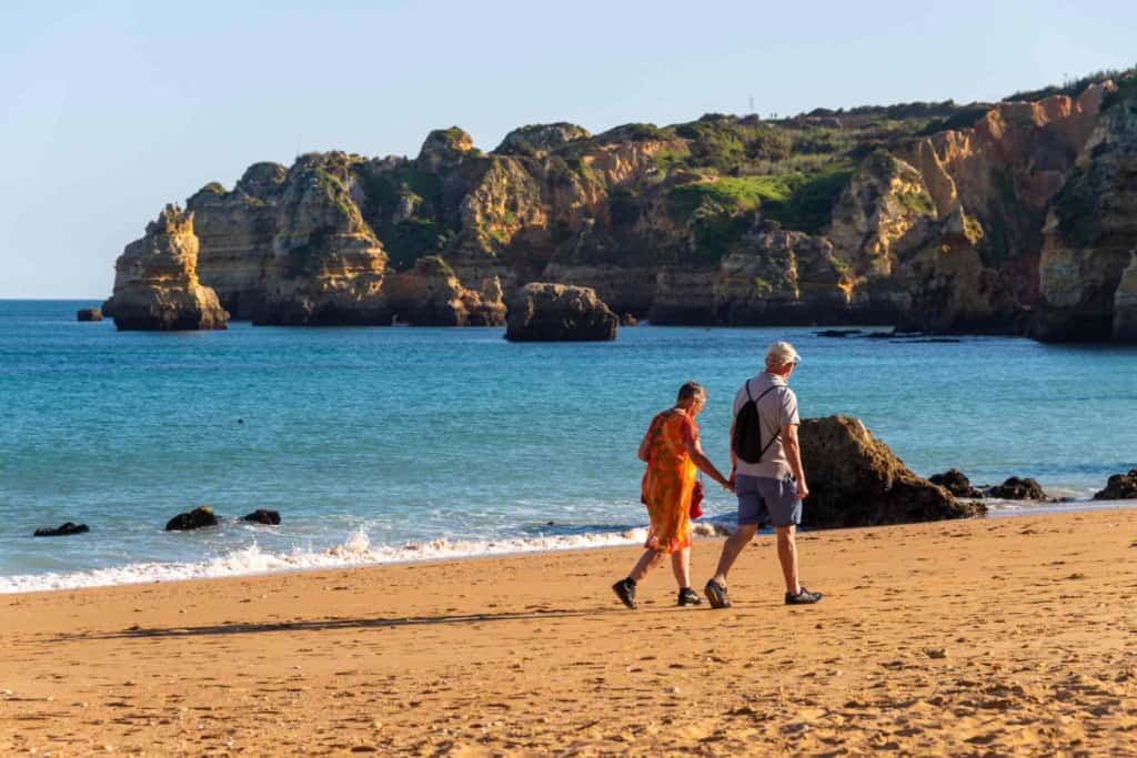 a senior couple walking along a beach in the Algarve, a popular location for retiring in Portugal