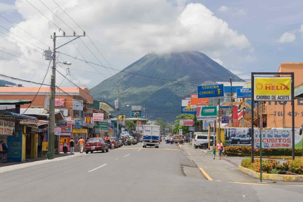 A vibrant street view with shops and signage in front of a volcano, highlighting travel destinations and the importance of international insurance coverage.