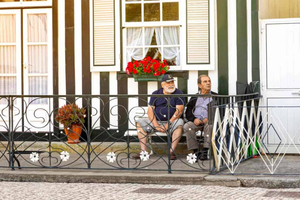 two Senior men relaxing next to a typical striped fishing houses in Aveiro, a popular location for retiring in Portugal