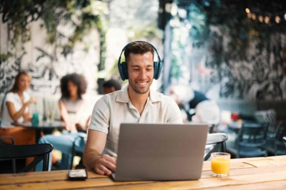 A smiling man wearing headphones works on his laptop at a cafe, illustrating international health insurance options valued by global travelers and expatriates.