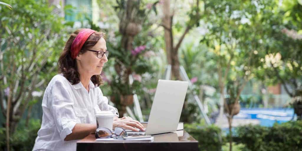 Photo of a woman working comfortably in a lush outdoor garden with her laptop, highlighting international insurance options for global residents.