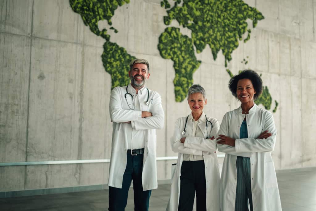 Diverse team of doctors standing confidently in a modern environment with a lush green world map background.