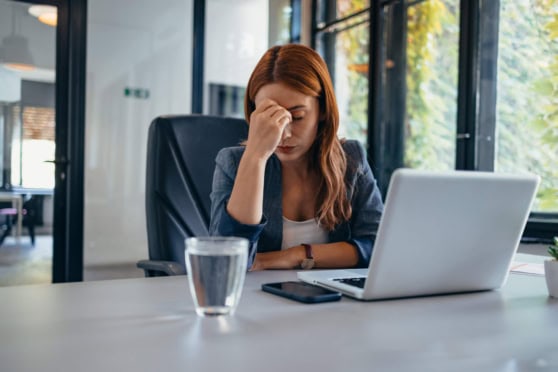 Frustrated woman with hand on forehead at desk with laptop and phone, feeling stressed while dealing with international insurance concerns.