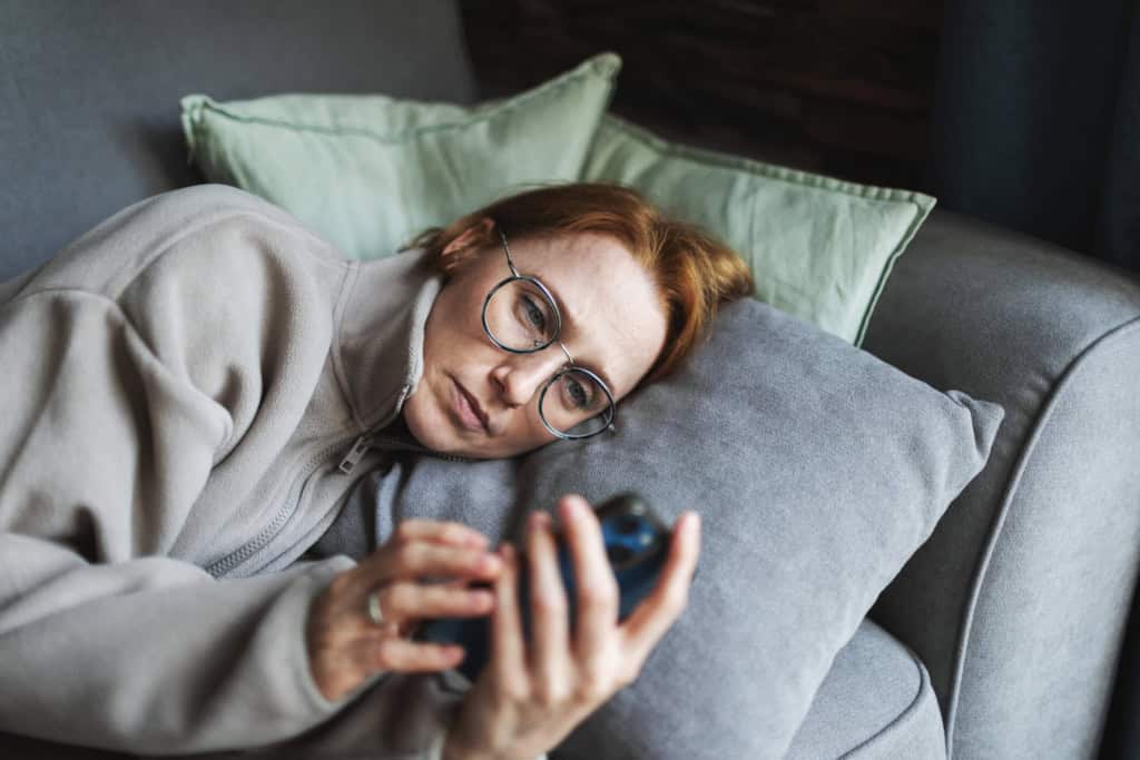 a woman looking tired and scrolling on her phone on the sofa
