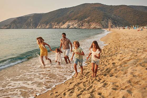 Family enjoying a beach vacation, with children and parents walking along the sandy shore, surrounded by calm ocean waters and scenic coastal landscape.