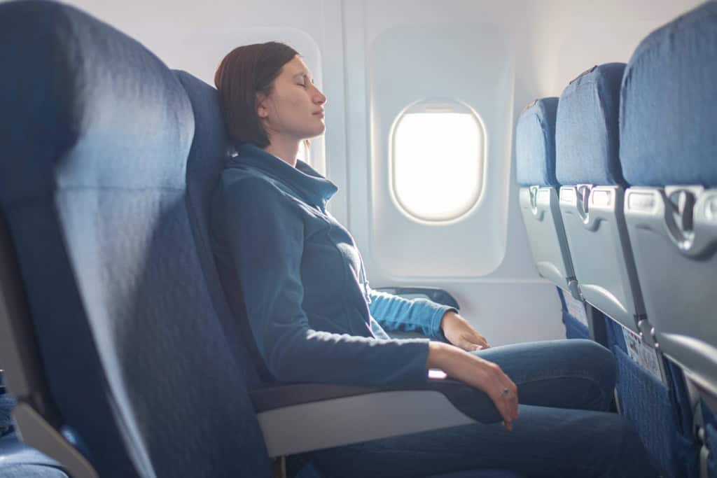 a female passenger sitting with her eyes closed in a window seat on a plane, hoping she is flying with one of the safest airlines