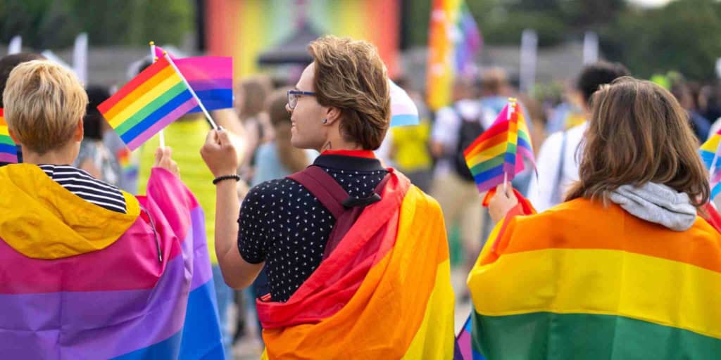 People holding rainbow pride flags at an LGBTQ+ pride event, emphasizing diversity, acceptance, and celebration of the LGBTQ+ community and the important question “where should I move”