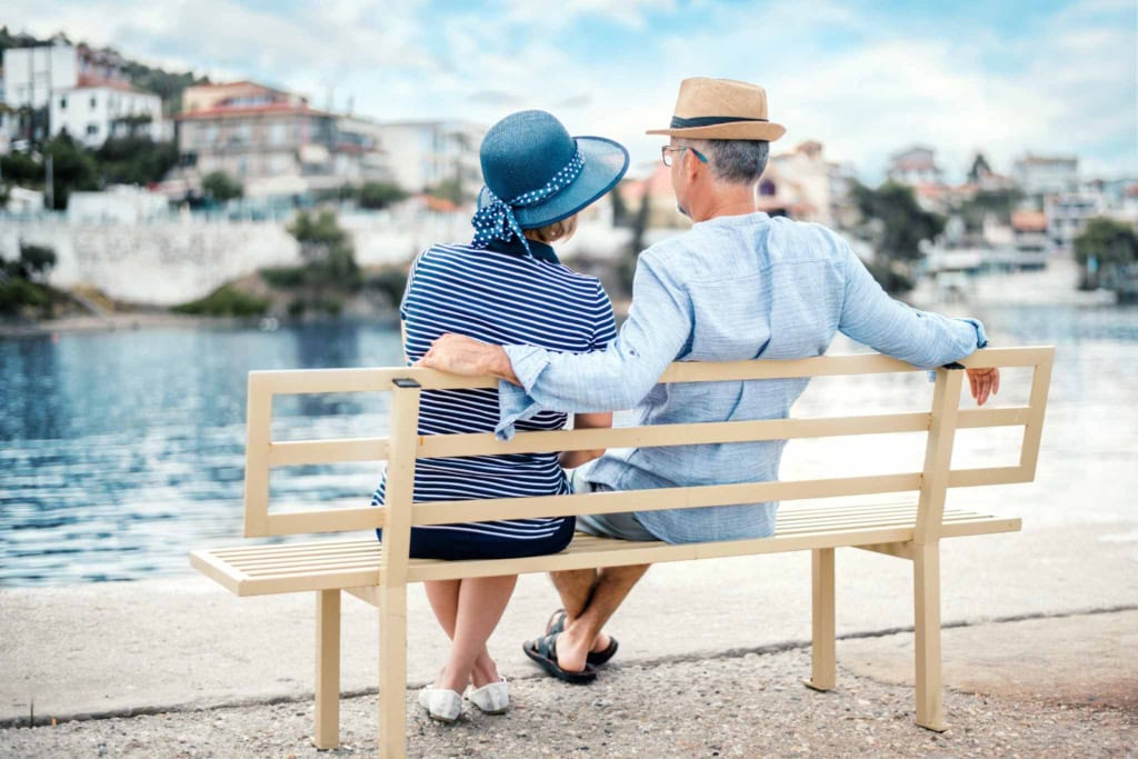 a happy couple sitting on a bench in Greece, one of the best places to retire in the world