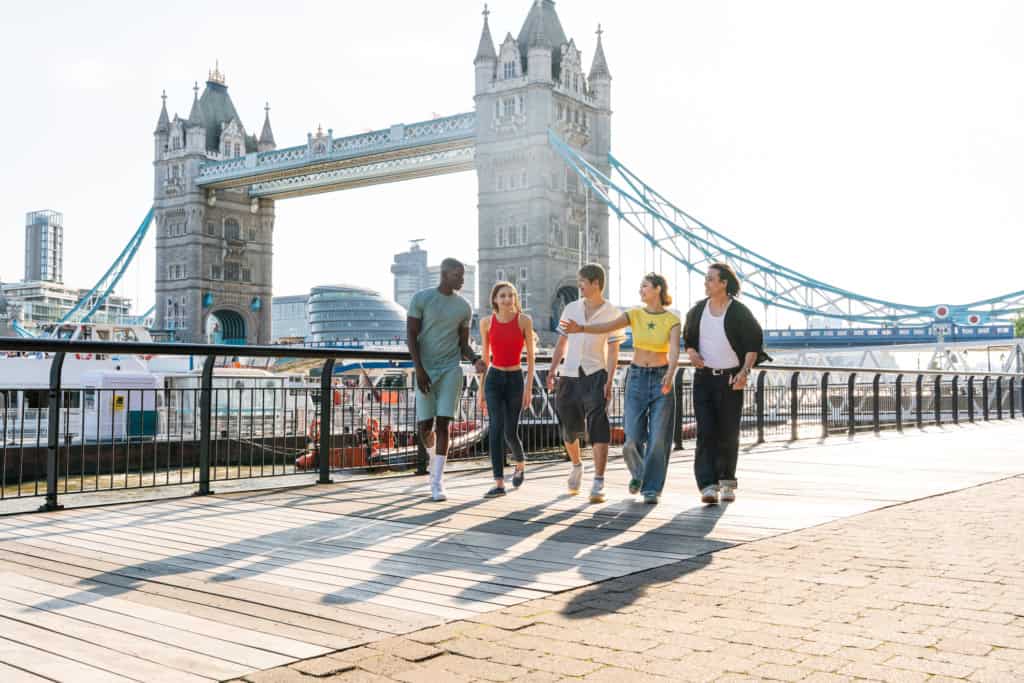 Diverse group of friends enjoying a walk along the London Thames riverside with iconic Tower Bridge in the background.