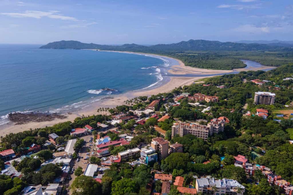 Aerial view of a beautiful beach town with turquoise waters, sandy shores, and surrounding greenery, highlighting international health insurance solutions for global citizens.