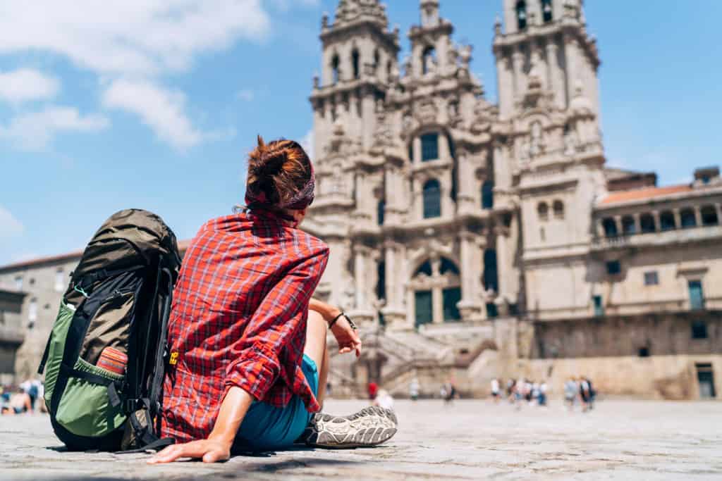 Woman tourist sitting on cobblestone plaza in front of historic cathedral, sightseeing, travel, exploring architecture, cultural tourism, backpacker, Germany, European landmarks, ICI conference destination.