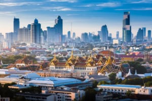 A panoramic view of Bangkok showcasing a blend of historic temples with ornate rooftops and modern skyscrapers in the background under a clear blue sky.