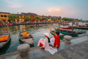 A picturesque riverside scene featuring traditional boats, colorful lanterns, and tourists enjoying the view in a vibrant Vietnamese town.