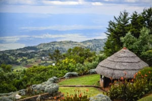 Roof hut situated on a lush hillside overlooking a vast, scenic landscape with rolling hills and greenery. The peaceful setting highlights natural beauty and tranquility.