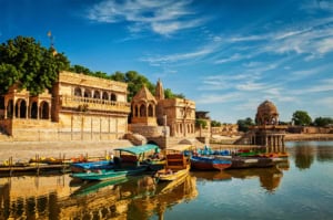 An image of historic Indian riverside architecture with ornate buildings and boats docked along the water.
