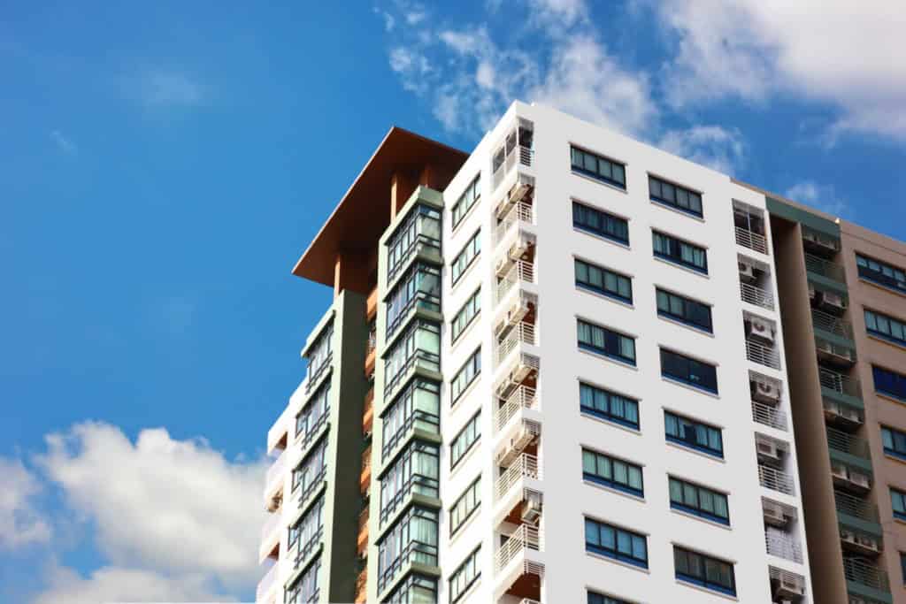 A contemporary high-rise apartment building in Thailand with large windows and balconies, set against a bright blue sky with scattered clouds, ideal for retirees seeking comfortable living options.