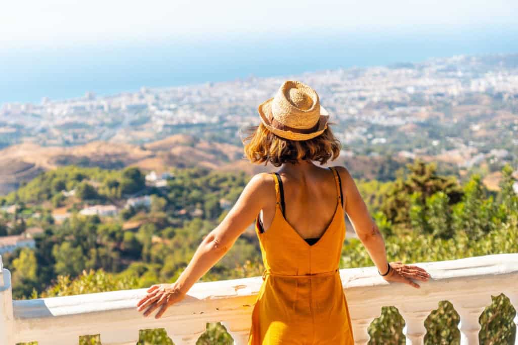 An expat woman enjoying a panoramic view of the coastline and cityscape from a scenic overlook, symbolizing the journey of becoming an expatriate and embracing a new lifestyle abroad.