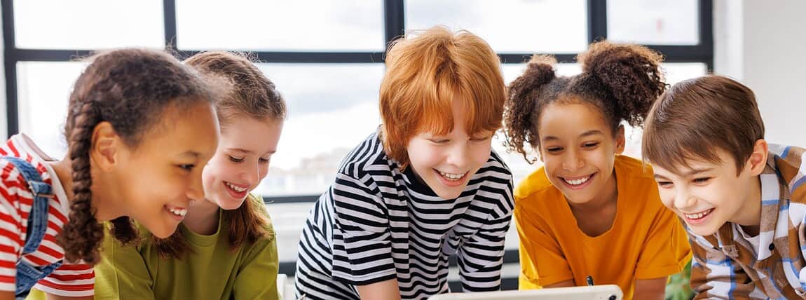 Group of diverse children engaging with a tablet during a classroom activity, promoting education abroad and international student health coverage.