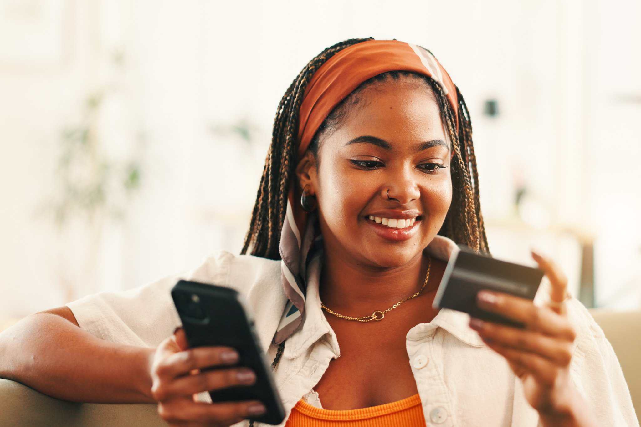 a smiling woman using her phone and credit card to manage her finances abroad
