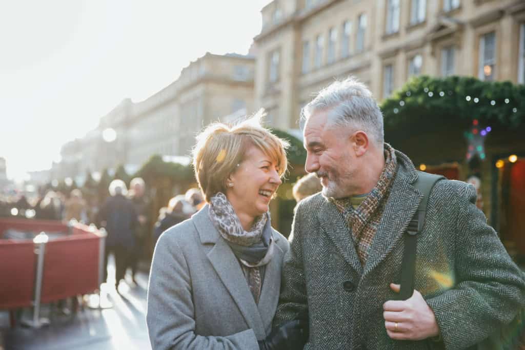 An elderly couple enjoying a sunny day in a UK city, smiling and engaging in conversation, highlighting the importance of international health and retirement insurance for expatriates.