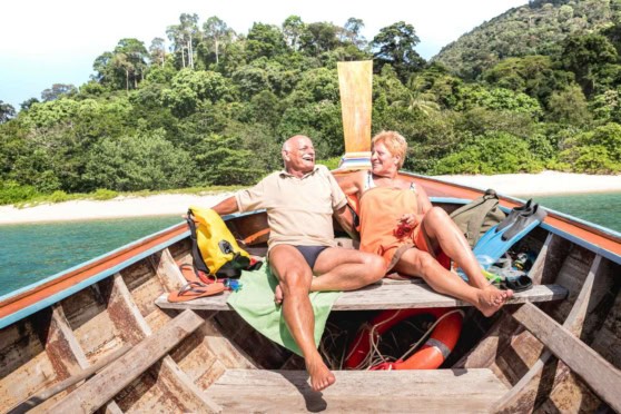An elderly couple enjoying a relaxing boat ride in Thailand, surrounded by lush green islands and clear blue waters, highlighting the appeal of retiring abroad.