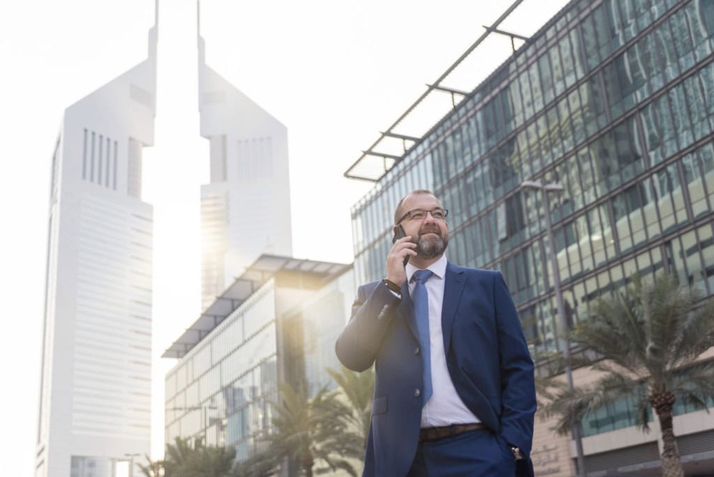 a businessman on his cell phone standing in front of a skyscraper in Dubai, UAE, one of the most popular expat countries with no income tax