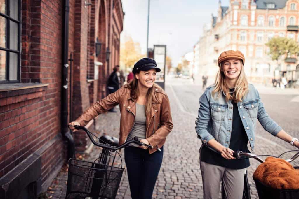 An image of two women walking and smiling in a Swedish city, showcasing a vibrant urban environment with historic buildings and cobblestone streets, ideal for retirees exploring city life.