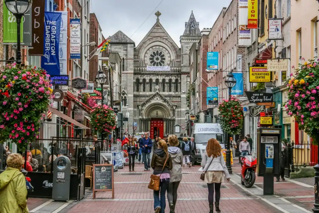 Historic city street with a prominent church in the background, bustling with pedestrians and colorful storefronts.