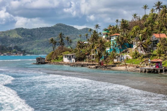 An image of a scenic coastal village in Panama featuring vibrant houses, palm trees, and lush hills in the background, highlighting the natural beauty and tropical environment of the area.