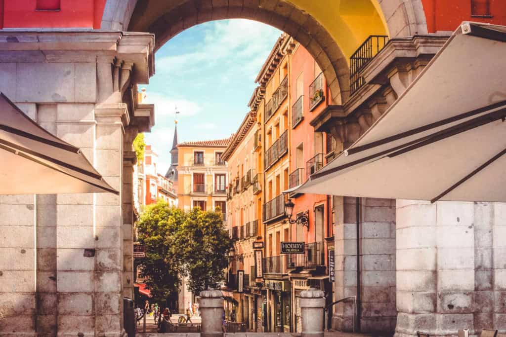 Scenic view of a historic Spanish city street framed by an archway, showcasing colorful buildings, outdoor cafes, and a lively atmosphere in the heart of Spain.