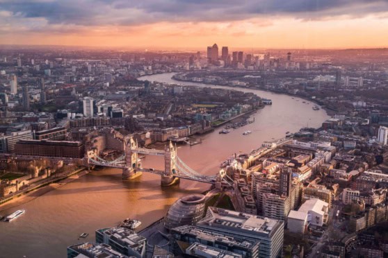 Aerial view of London showing Tower Bridge, the River Thames, and the city's skyline during sunset.