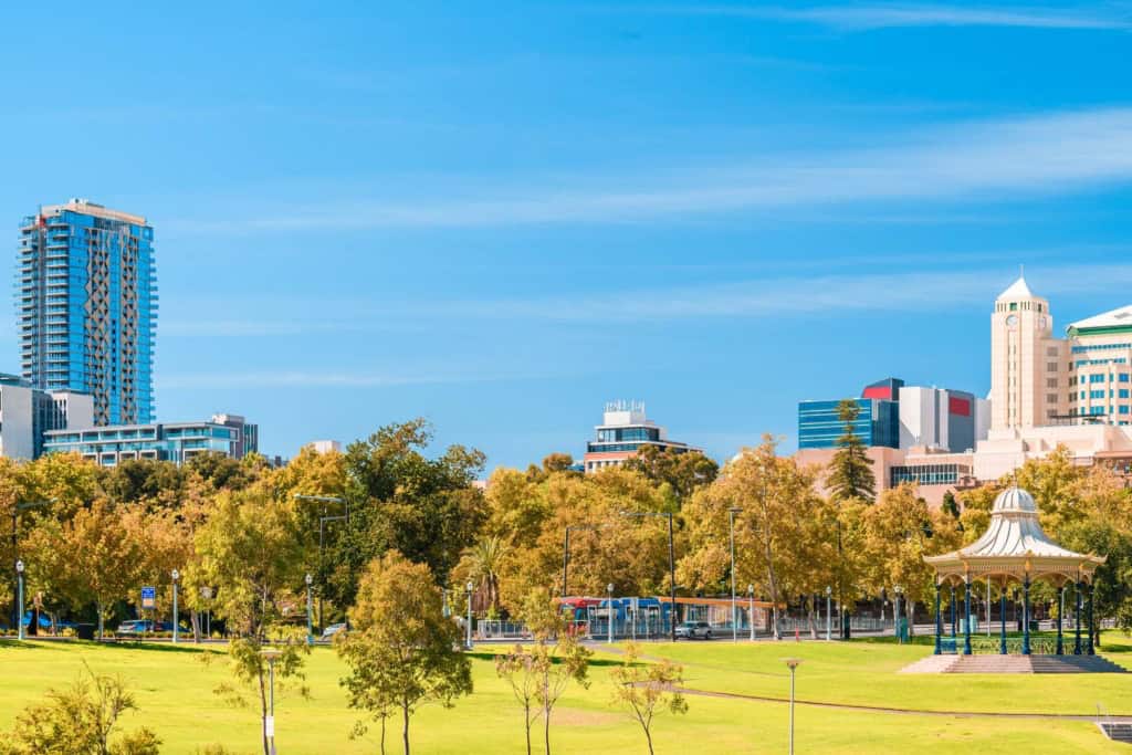 A scenic view of a city park in Australia featuring green lawns, trees, and a skyline with high-rise buildings under a clear blue sky.