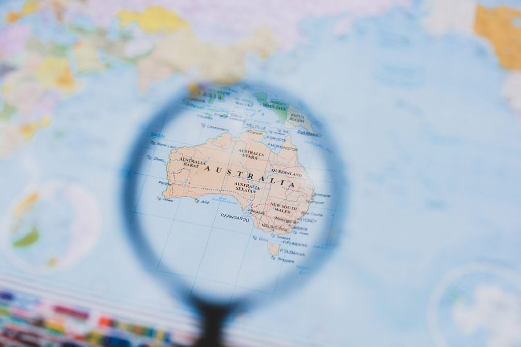 Close-up of a map highlighting Australia viewed through a magnifying glass, symbolizing focus on Australian citizenship and immigration processes.