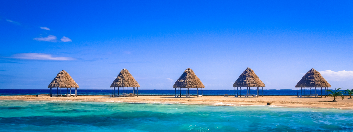 Beach huts on a tropical shoreline with clear blue water and sky.