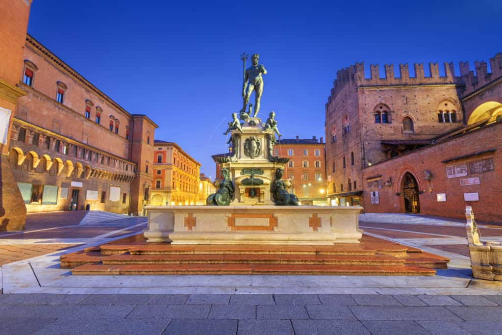 Historic fountain in a charming Italian square at dusk, with medieval buildings and a clear blue sky, perfect for newcomers planning their move to Italy.