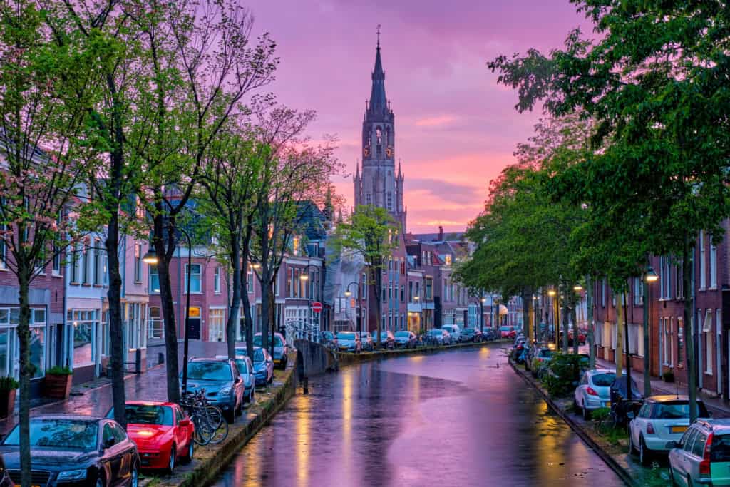 Beautiful view of a Dutch city street with historic buildings and a church tower at sunset.