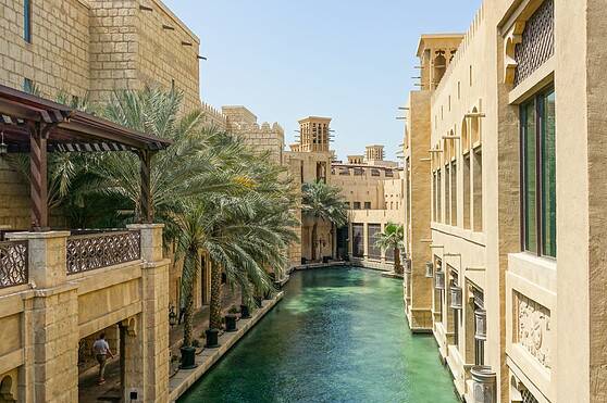 An elegant canal lined with historic sandstone buildings and lush palm trees, showcasing traditional architecture and serene waters in a vibrant Middle Eastern urban setting.